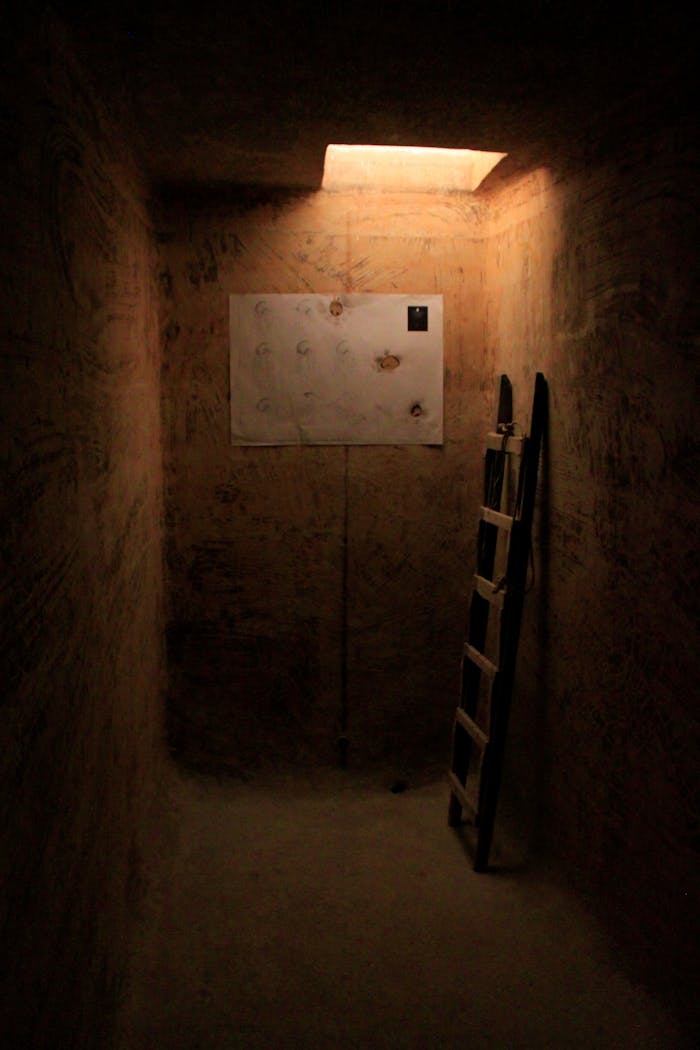 Dimly lit interior with ladder leading to a bright opening and art canvas.